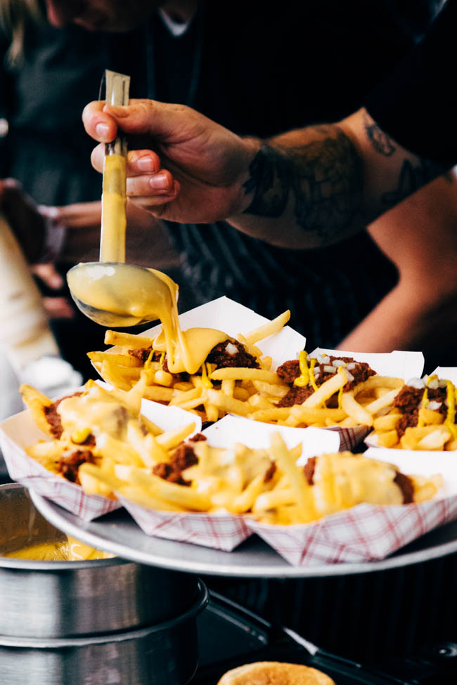 A ladle pouring cheese sauce over a platter of french fries.