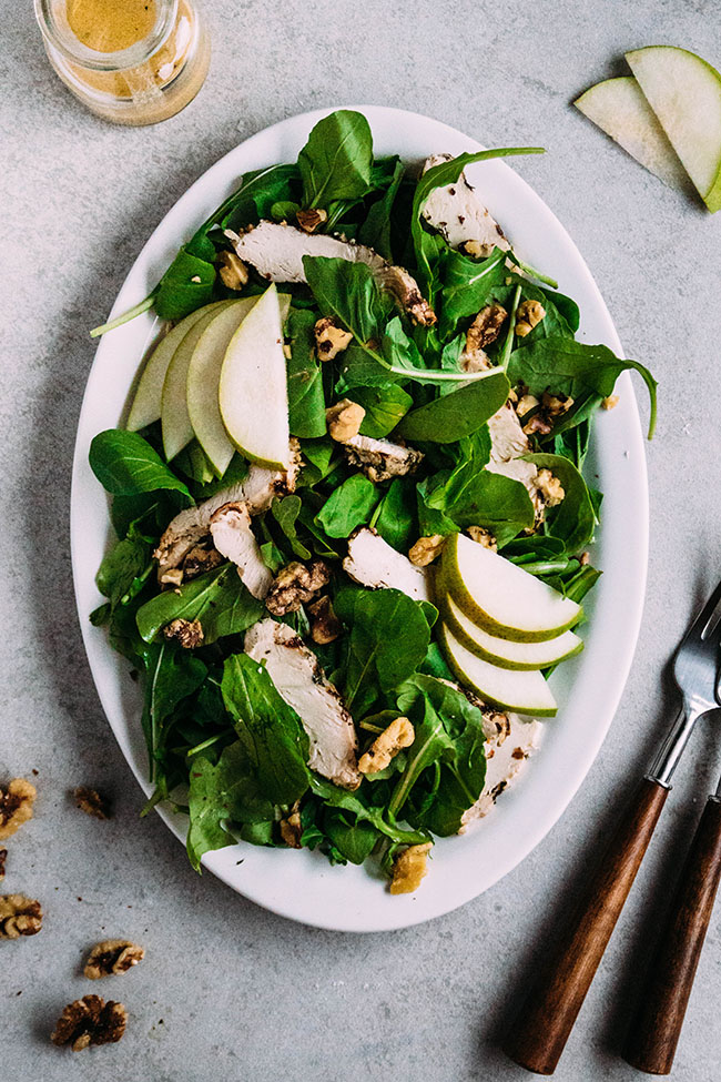White platter of arugula salad topped with sliced pears and walnuts.