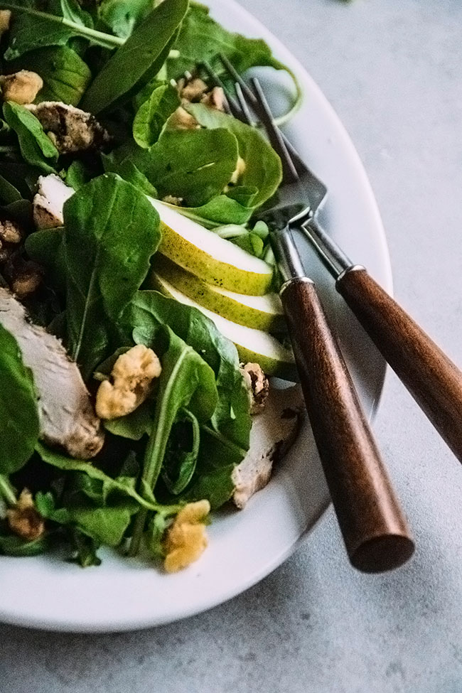 Close up of two wooden serving forks tucked into a plate of arugula salad.