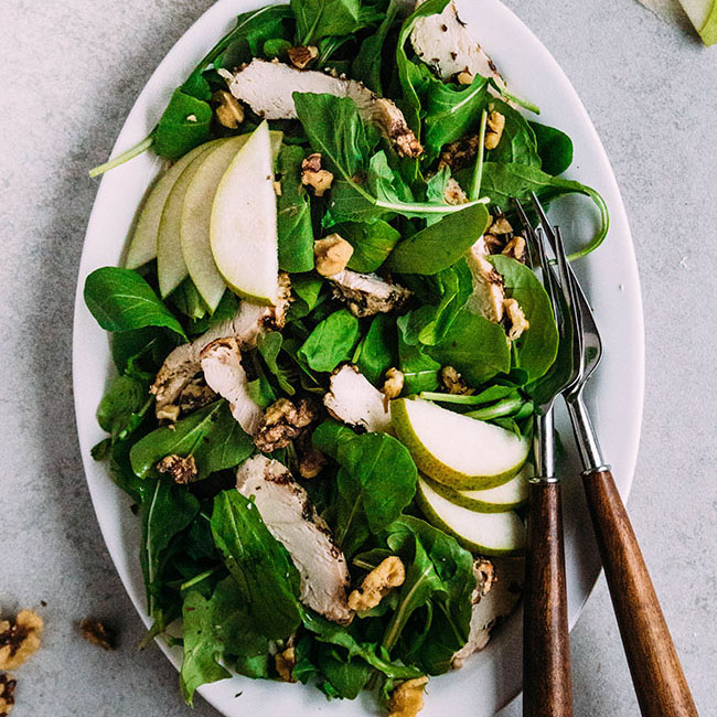 Arugula salad with pears and walnuts on a white plate.