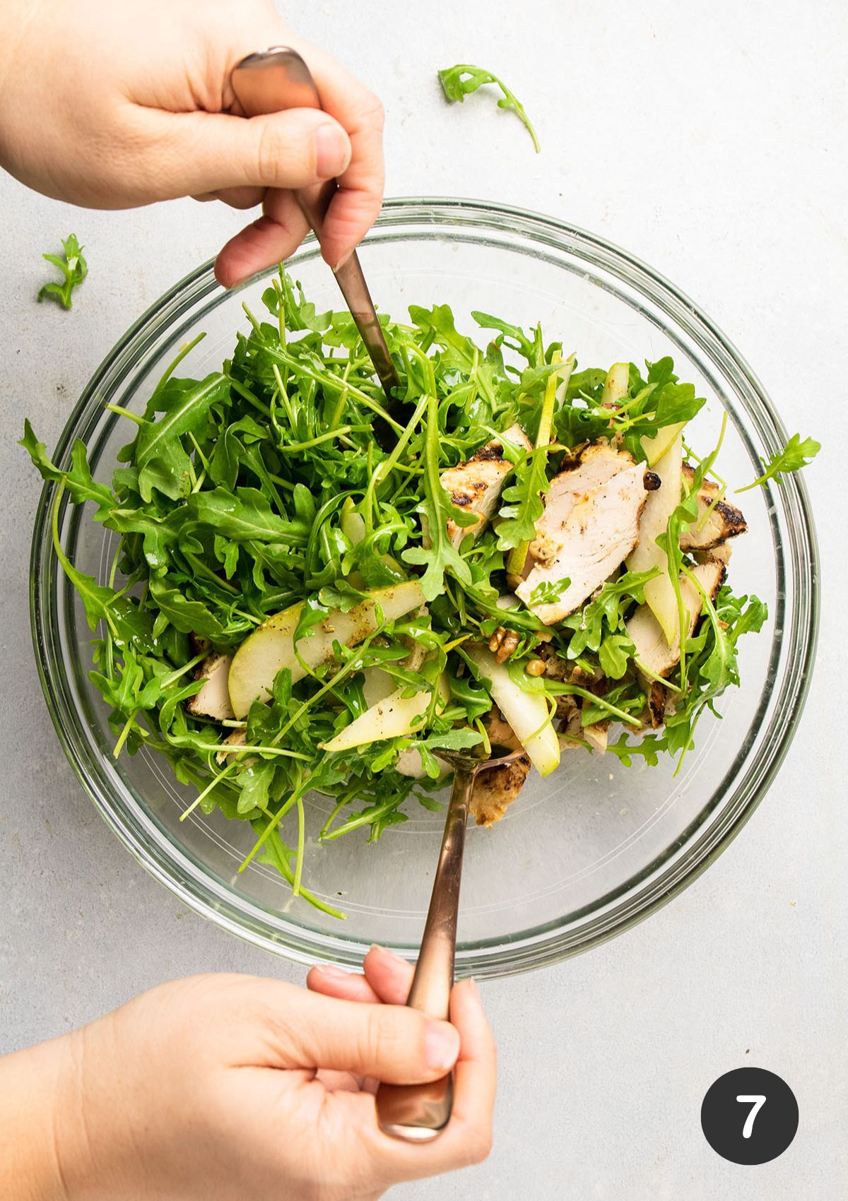 Tossing arugula chicken salad with two large forks.