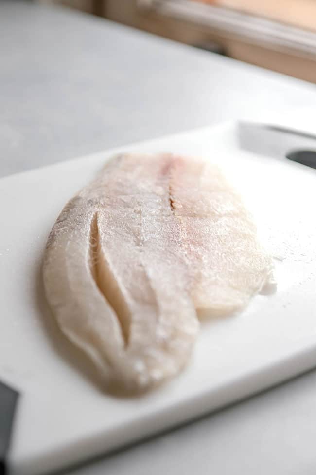 Uncooked barramundi fish fillet on a white cutting board.