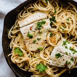 Spaghetti in a cast iron skillet topped with white fish and parsley.