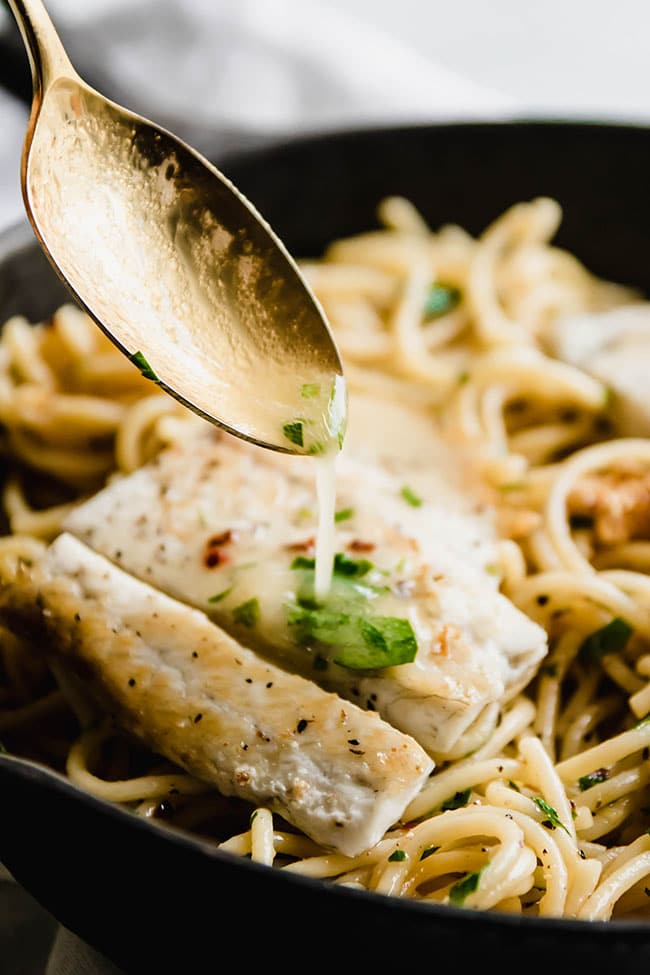 Gold spoon pouring melted butter over barramundi and spaghetti.