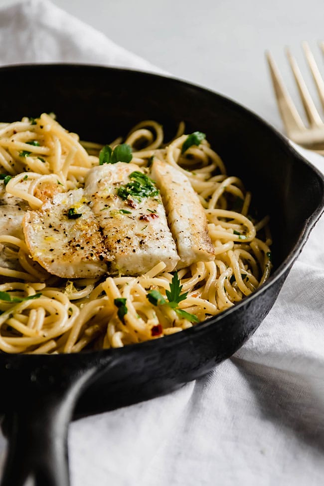 Cast iron skillet filled with pasta and seared white fish.