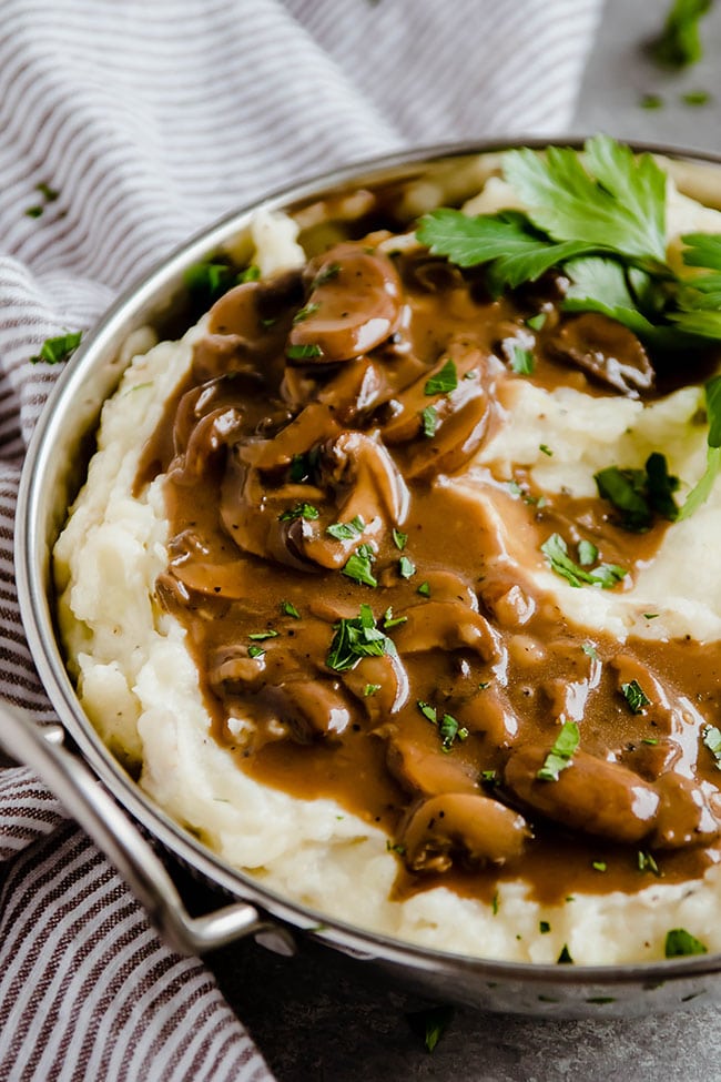 Mashed potatoes in a metal pot topped with mushroom gravy and fresh parsley.