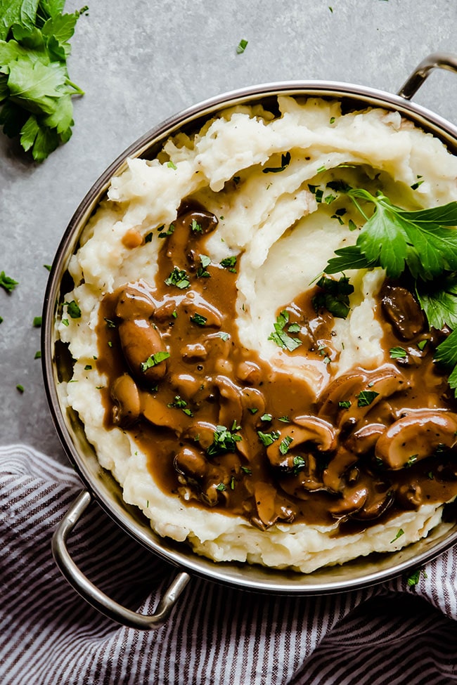 Mashed potatoes topped with mushroom gravy and parsley in a metal pot.