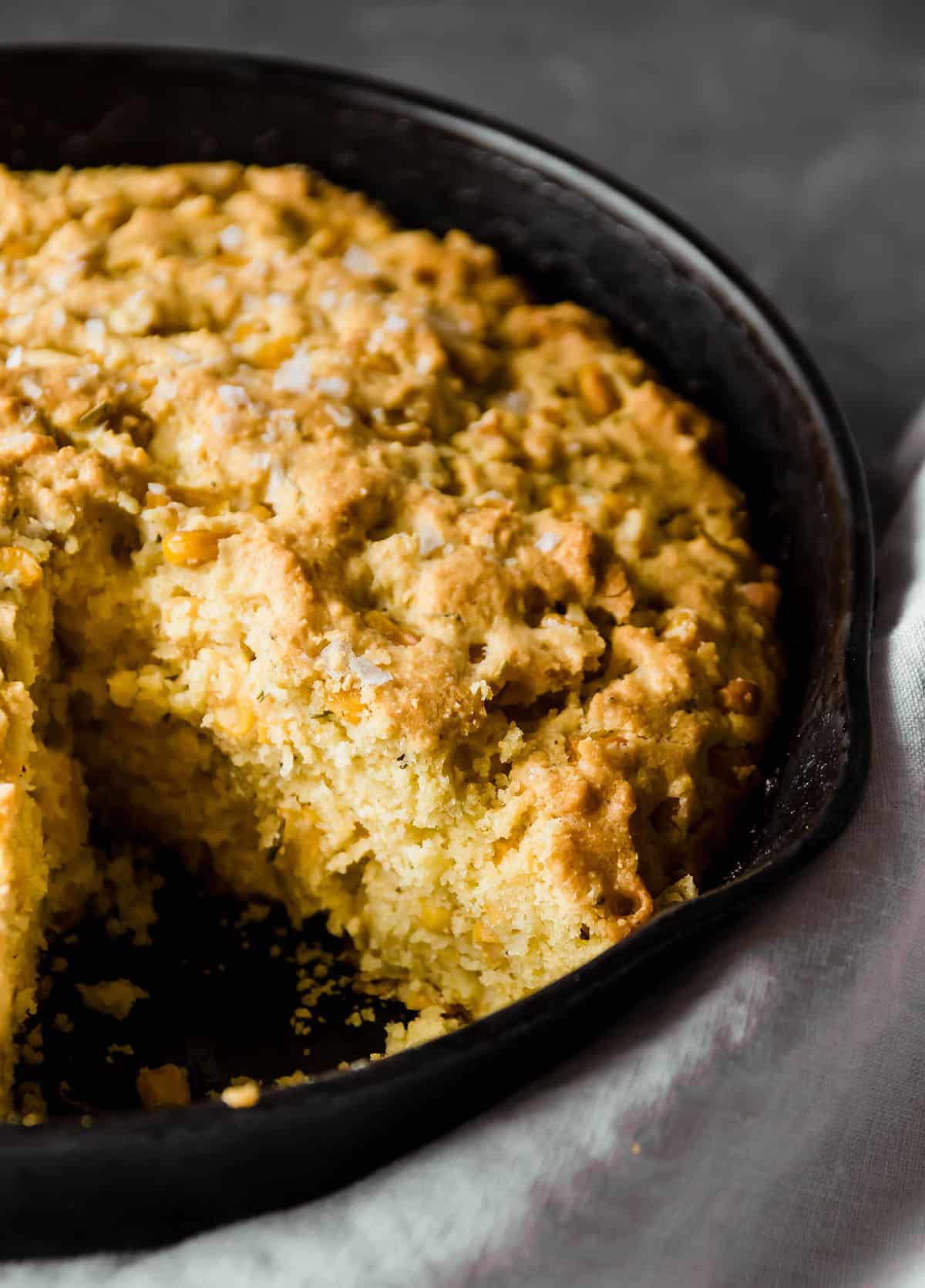 Fresh cornbread in a cast iron skillet with one piece missing.