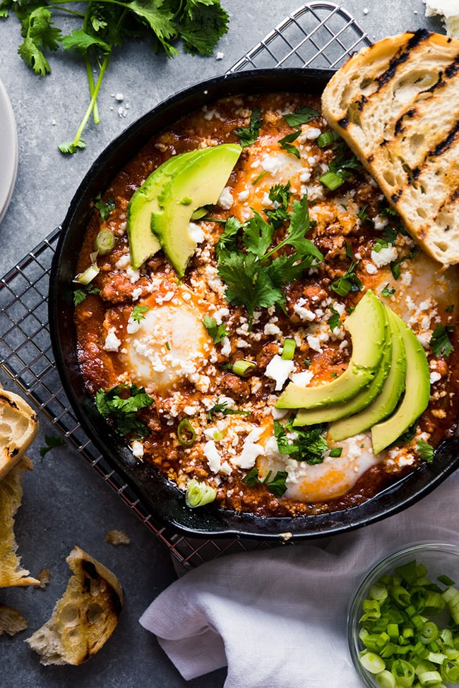 Baked eggs in tomato sauce, topped with avocado slices, fresh cilantro, and cotija cheese.