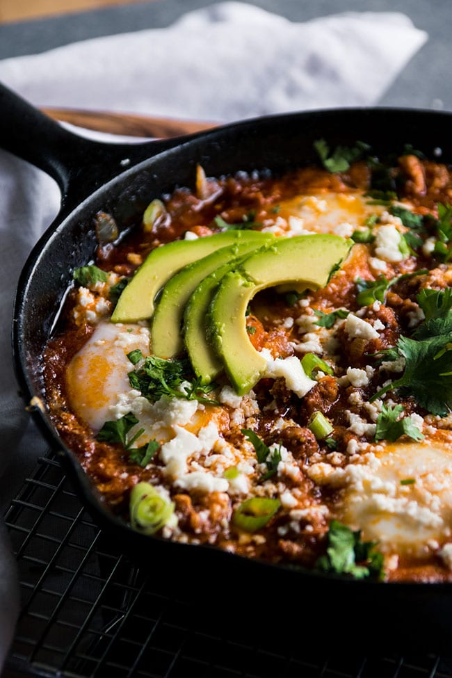 Baked eggs and tomato sauce in a skillet topped with avocado slices.