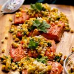 Four pieces of salmon topped with corn salsa on a wooden cutting board.