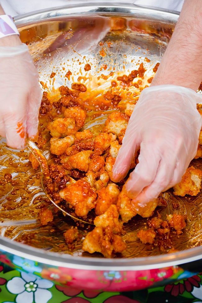 Hands mixing a bowl of fried cauliflower with buffalo sauce.
