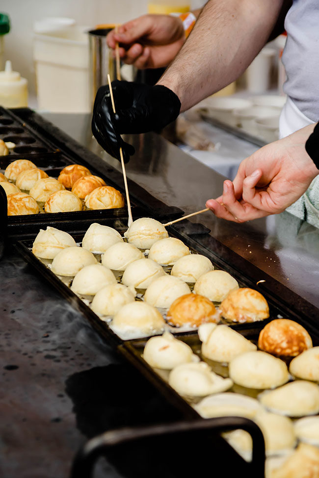 Hands flipping round pastries over a griddle.