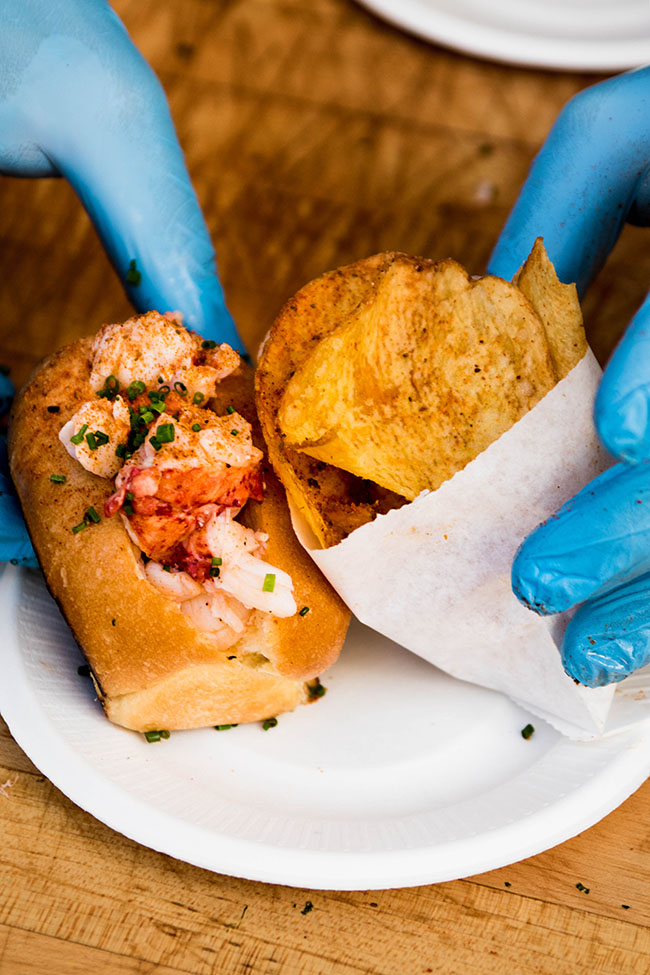 Mini lobster roll next to fresh potato chips on a white appetizer plate.