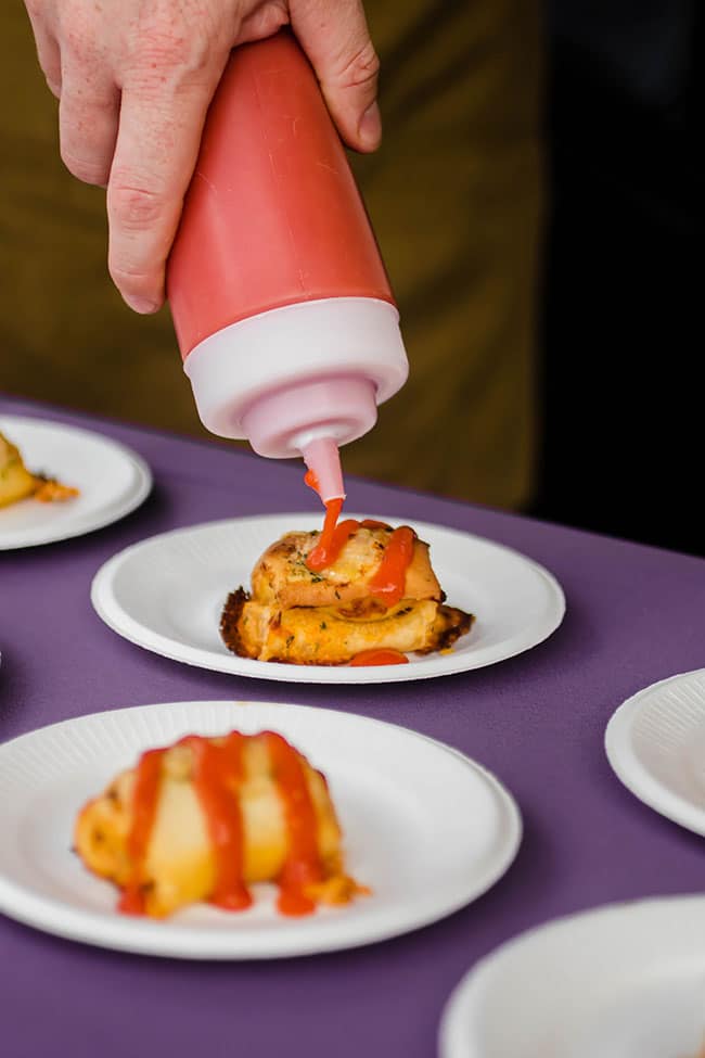 Hot sauce being poured out of a squeeze bottle onto a hot pocket.