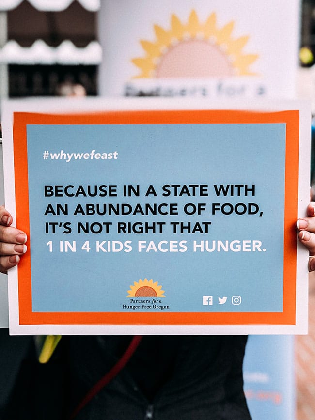 Woman's hands holding a poster that says 'because in a state with an abundance of food, it's not right that 1 in 4 kids faces hunger.'