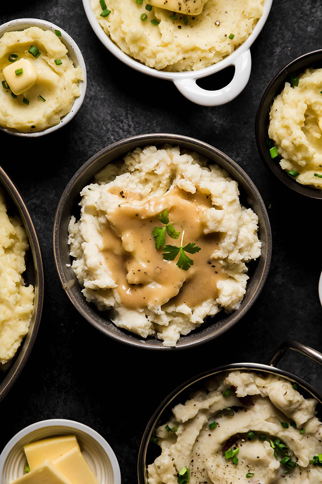 Bowl of mashed potatoes and gravy on a dark table.