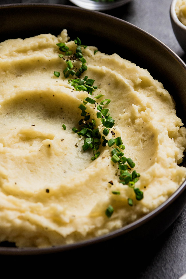 Mashed potatoes swirled into a black bowl and topped with chopped chives.