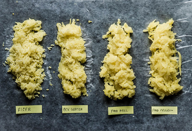 Four piles of cooked potatoes, shredded with various methods to show the difference in texture from a ricer, box grater, food mill, and food processor.