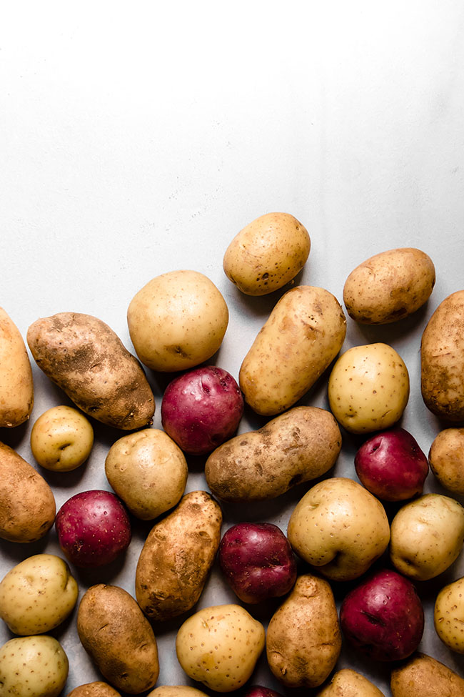 Multiple whole potatoes in varying colors on a white background.