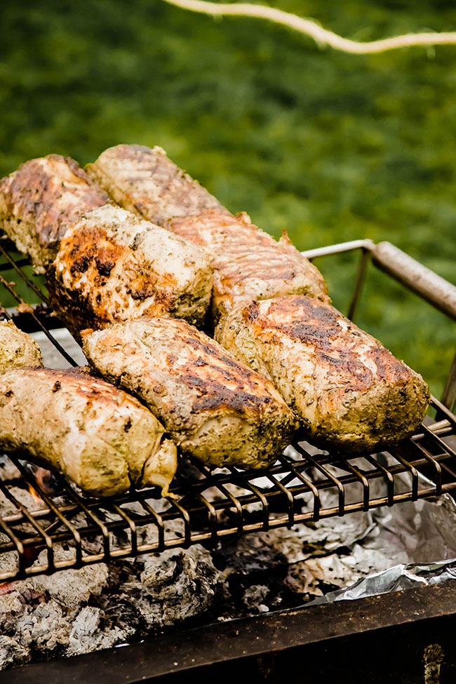Several large pork shoulders cooking over a large grill.
