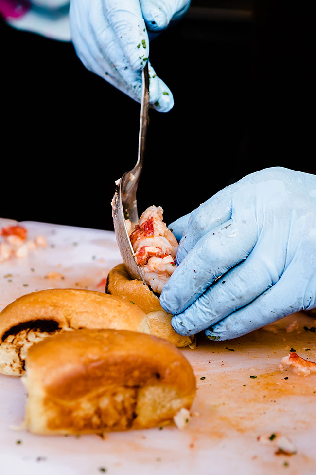 Hands in blue gloves stuffing lobster into a small roll.