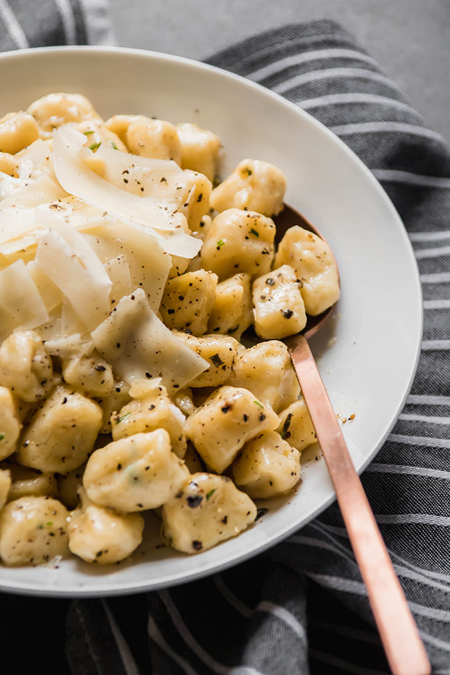 Fresh gnocchi topped with parmesan cheese in a white bowl with a copper spoon.
