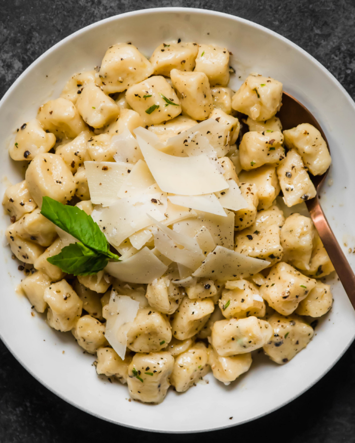Gnocchi with shaved parmesan in a shallow white bowl on a dark table.