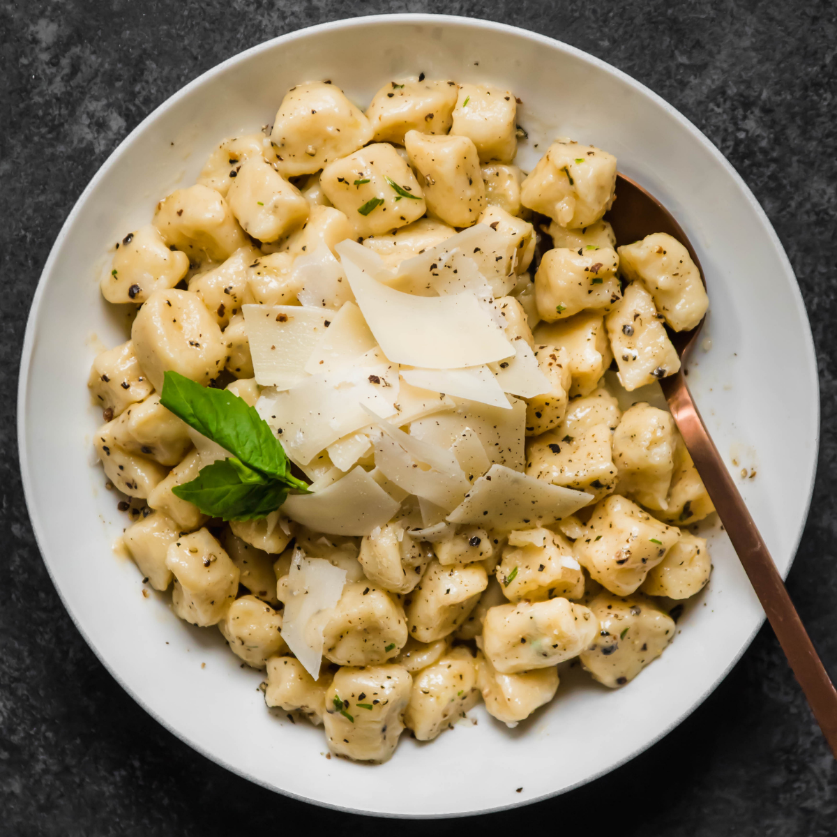 Gnocchi with shaved parmesan in a shallow white bowl on a dark table.