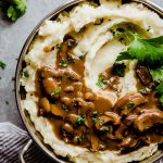 Overhead photo of mashed potatoes in a silver bowl with mushroom gravy and parsley on top