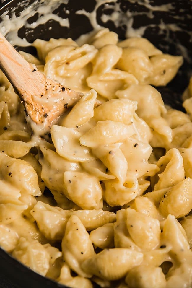 Wooden spoon stirring macaroni and cheese made with shell pasta.