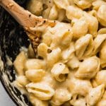 Wooden spoon stirring macaroni and cheese in a large pot.