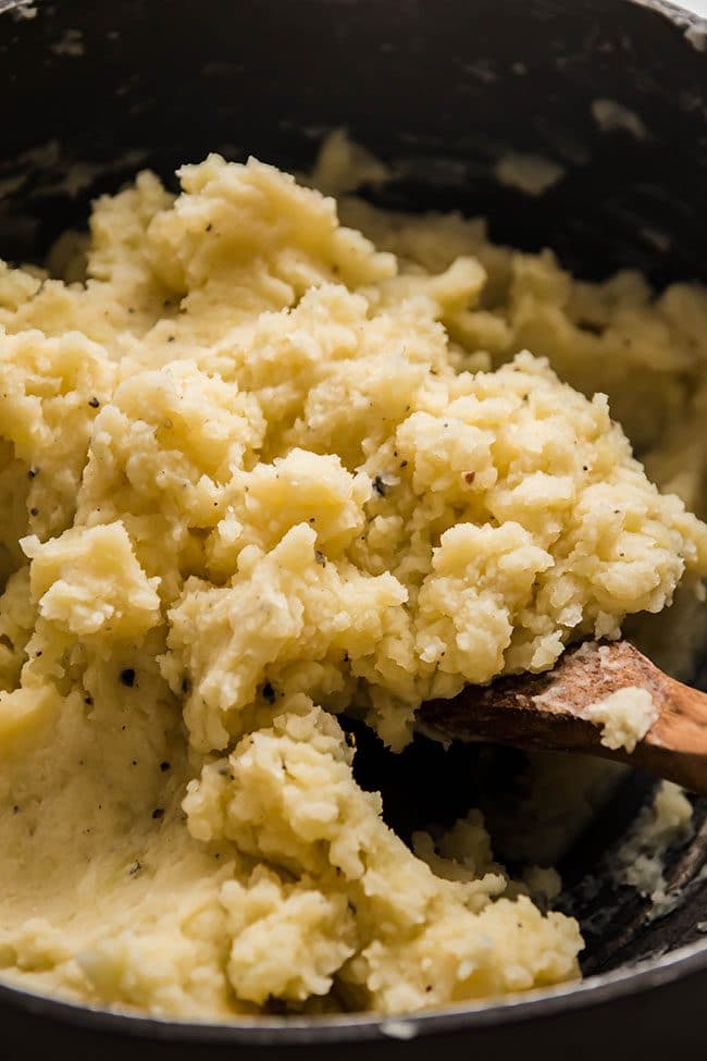 Wooden spoon stirring cauliflower mashed potatoes in a large pot.
