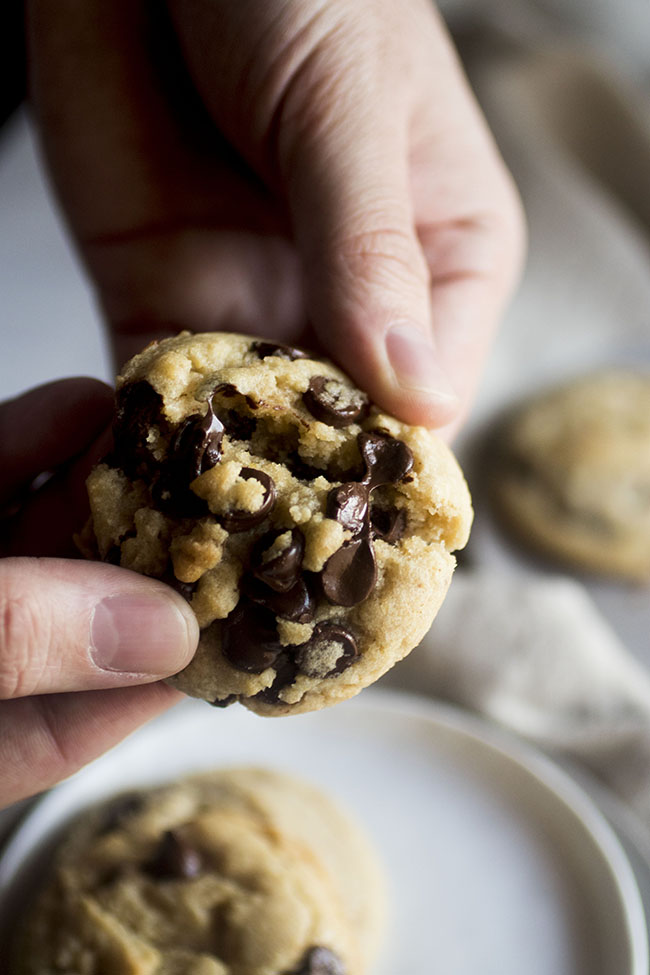 Hands breaking a fresh chocolate chip cookie in half.