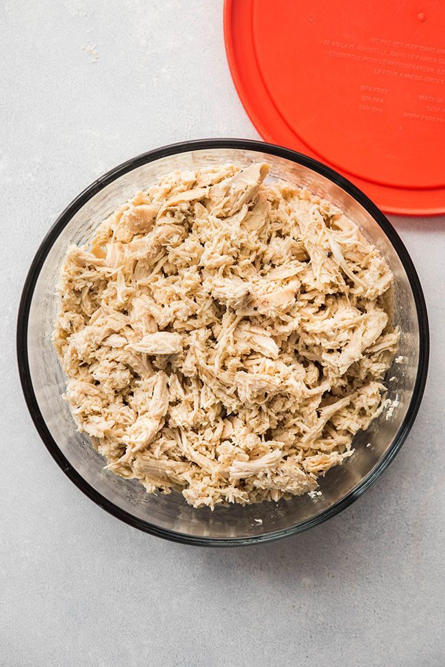 Shredded chicken in a glass container next to a red lid.