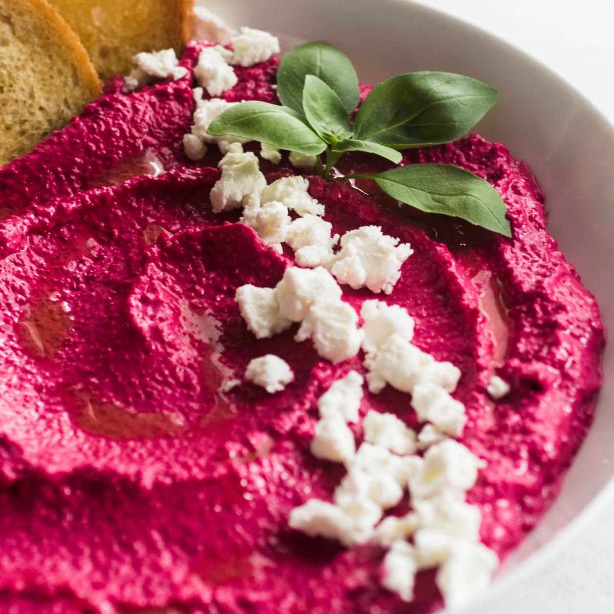 Pink beet dip in a white bowl topped with fresh basil.