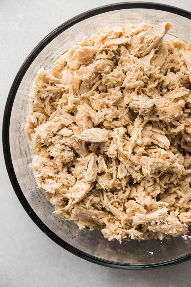 Close up of shredded chicken in a glass bowl.