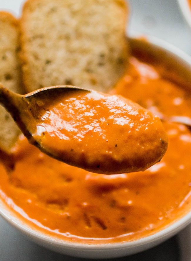 Spoon lifting a bite of tomato soup out of a white bowl.