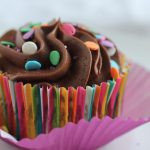Chocolate cupcake in a bright striped wrapper with chocolate frosting and sprinkles.