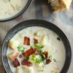 Clam chowder topped with crispy bacon in a black bowl.