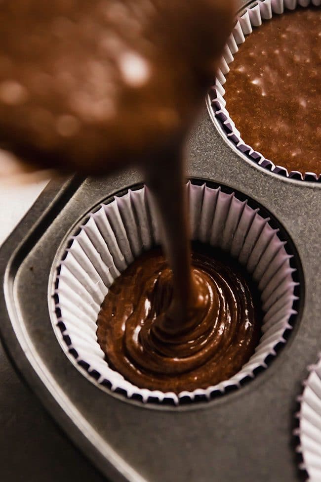 Chocolate cake batter being poured into a cupcake liner.