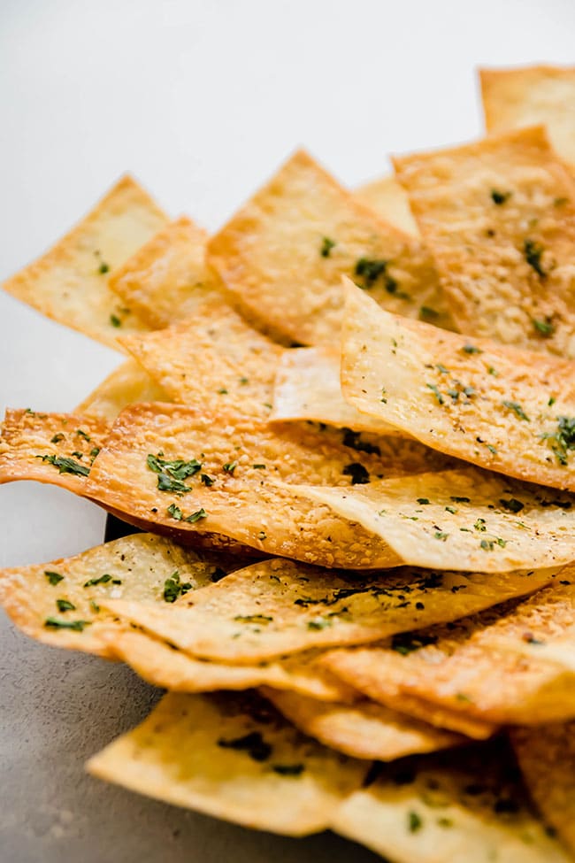 Thin parmesan wonton crackers in a pile on a black plate.