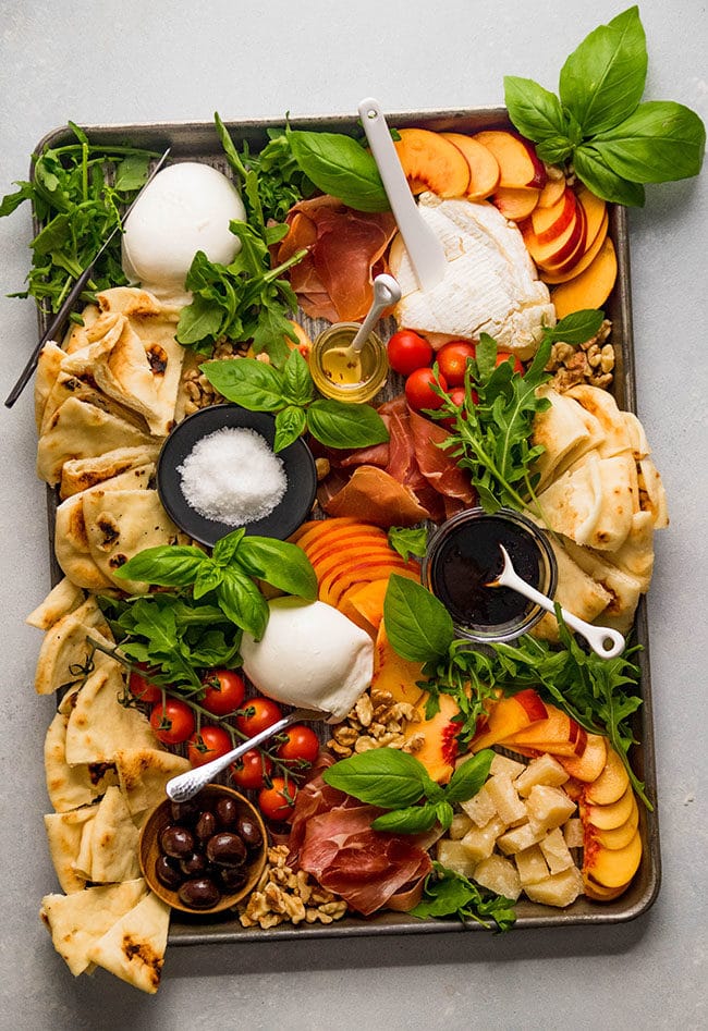 Various cheeses on a sheet pan with peaches, tomatoes, and basil.