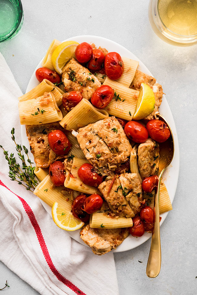 Barramundi pasta with tomatoes and lemon wedges on a large white serving platter.
