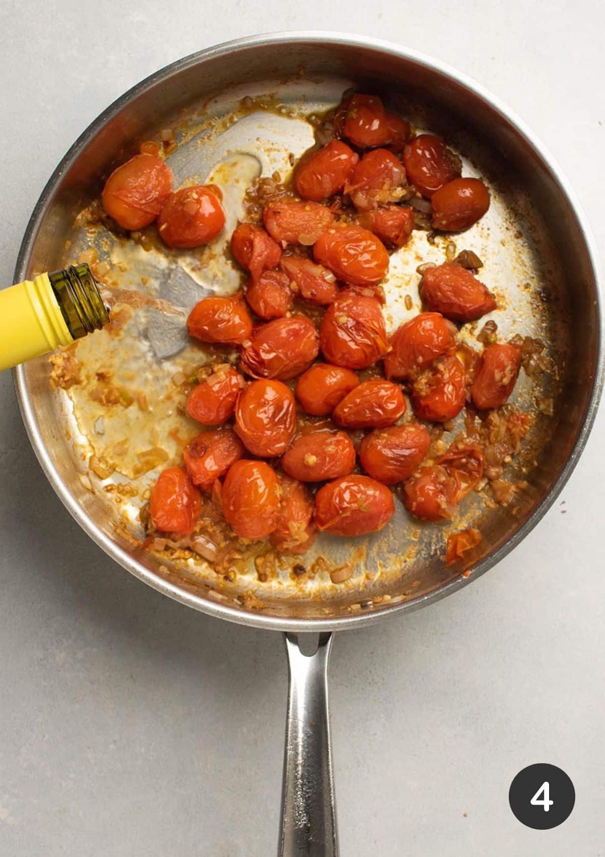 Pouring white wine into a skillet with burst tomatoes.