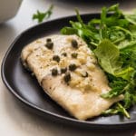 Baked fish on a black plate with fresh arugula.