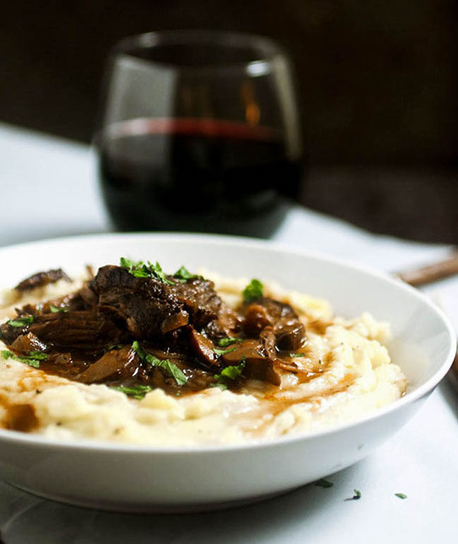 Braised beef short ribs and mashed potatoes in a shallow white bowl on a dark background.