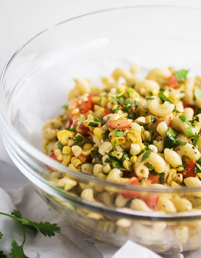 Pasta salad in a glass bowl with grilled corn and diced tomatoes.