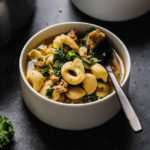 Tortellini soup with sausage and kale in a white bowl.