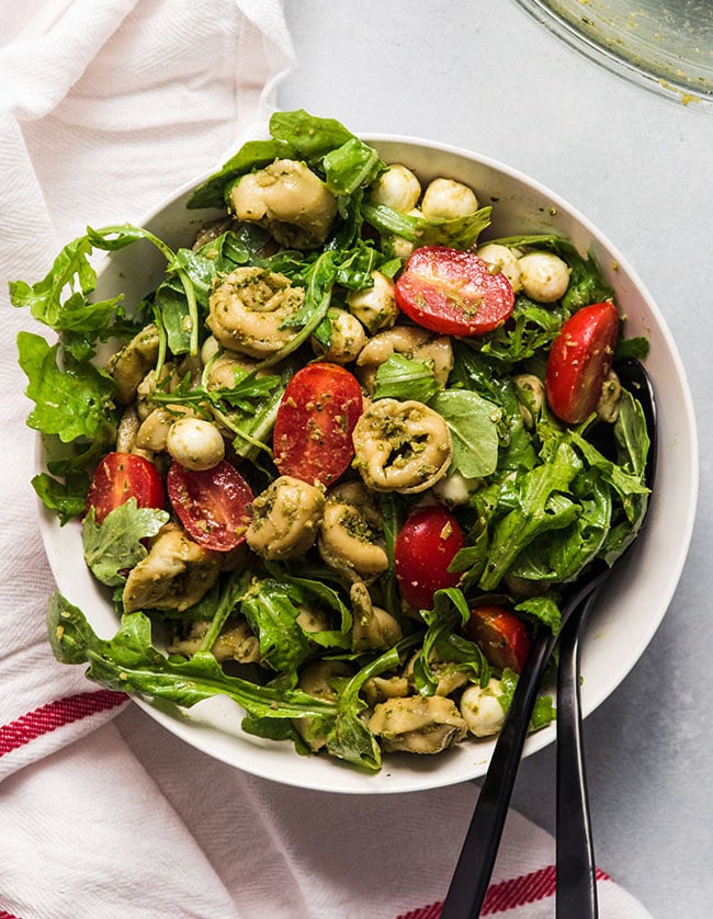 Cheese tortellini salad in a white bowl with arugula and tomatoes.